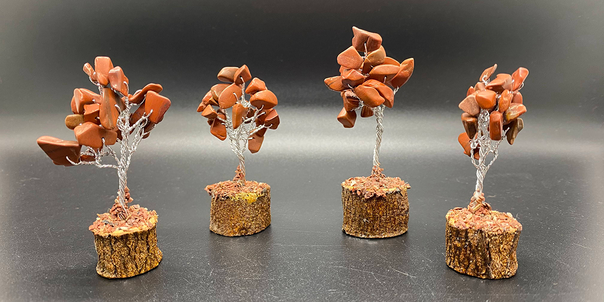 Four mini red jasper crystal trees on a black background. Each tree has a wooden base, a silver wire trunk and branches, and red jasper stone chips at the ends of each branch.. 