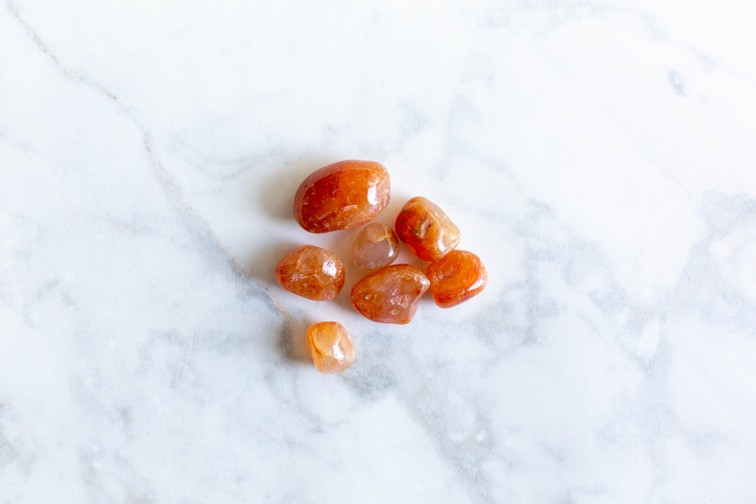 7 small carnelian tumbled stones together on a white marble background